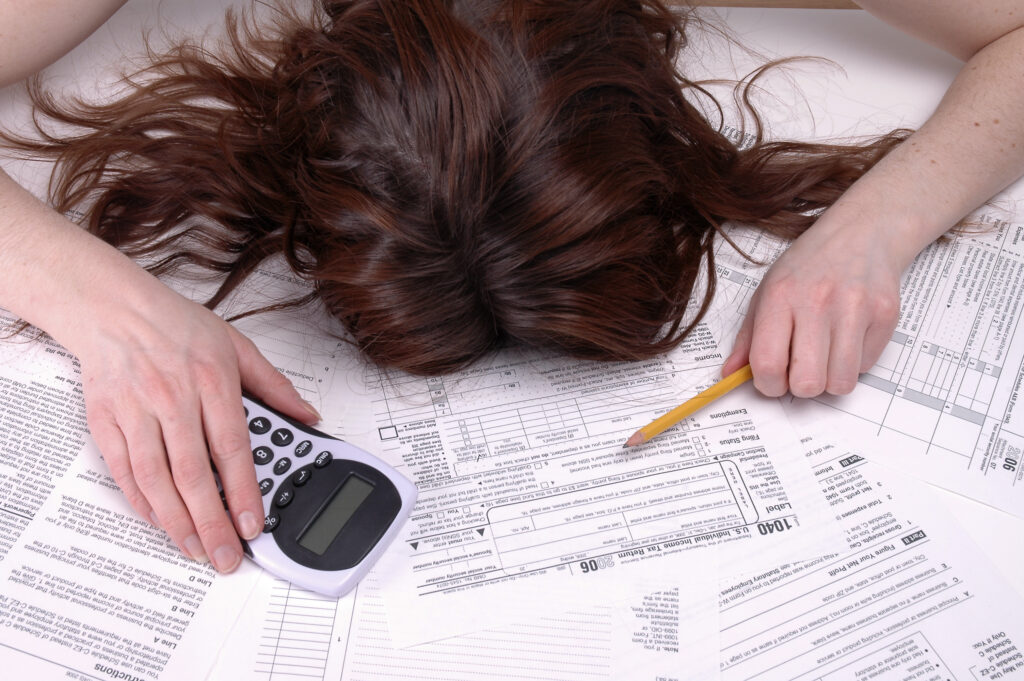 a woman with her head on a lot of paperwork, next to a calculator 